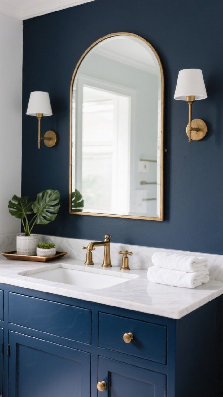 Medium bathroom vanity closeup: freshly painted vanity in deep navy enamel with smooth, durable finish; matching brushed brass hardware and faucet; twin sconces mounted at 62 inches on either side of a framed arched mirror for flattering light; styled with a small tray, a leafy plant, and plush white towels; crisp, spa-like ambiance.