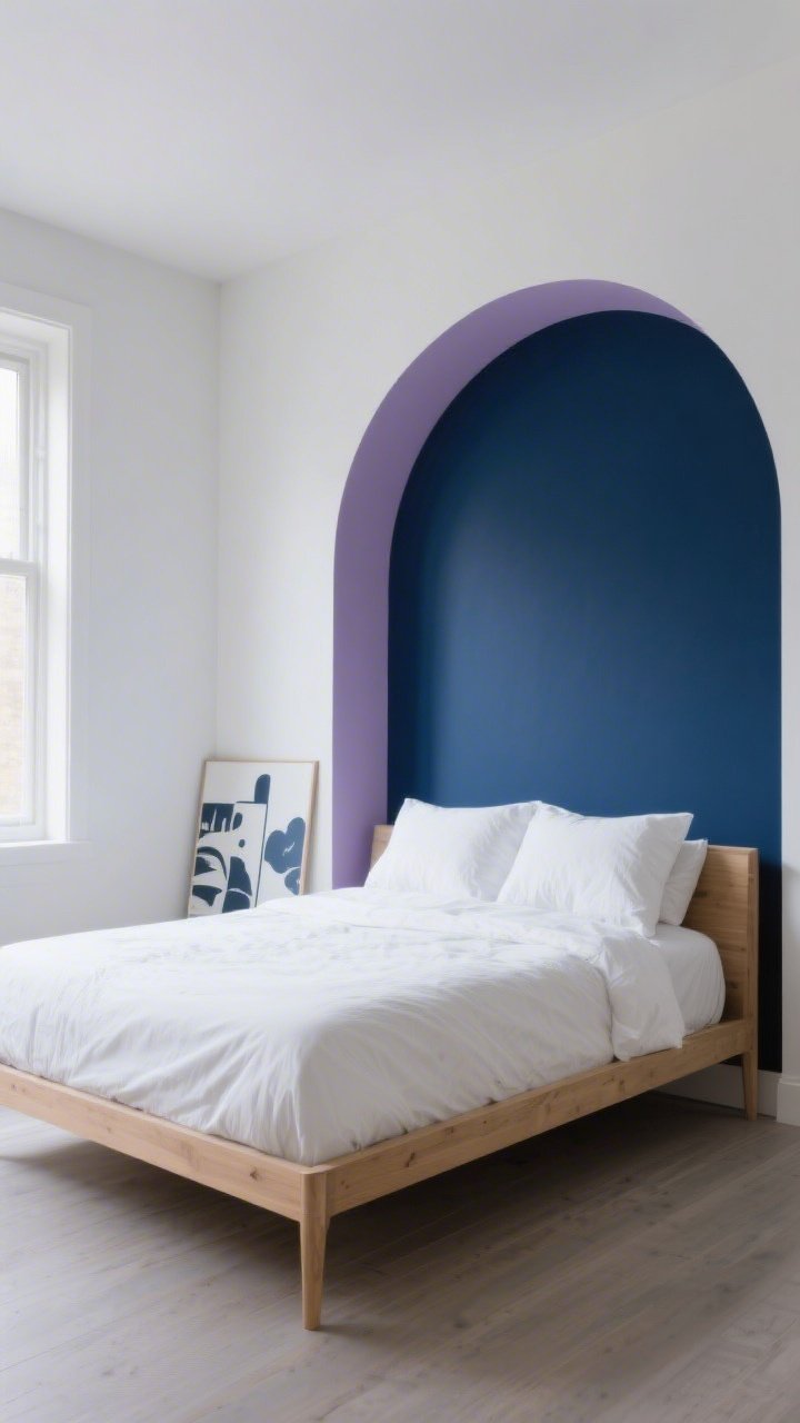 Wide shot of a modern bedroom with a single bold accent wall painted deep moody navy behind the bed, the other walls soft white; subtle color-blocked half-arch in dusty mauve overlapping one corner of the navy wall; natural morning-to-evening lighting gradient visible on paint; minimal decor with a light wood bed frame, crisp white bedding, and a few peel-and-stick mural panels leaning nearby to imply renter-friendly options; straight-on view, photorealistic.