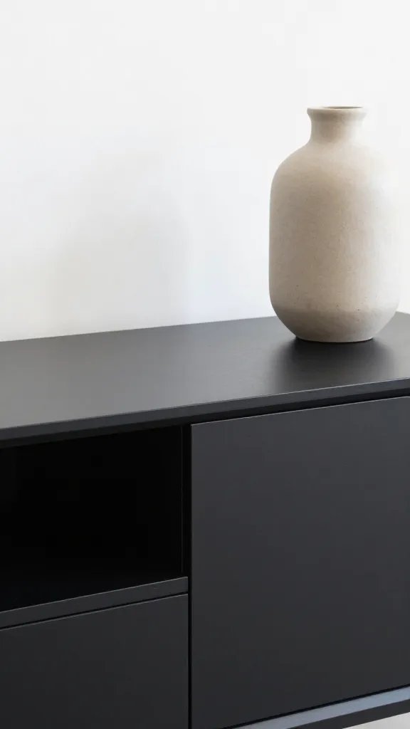 closeup of a matte black TV stand edge paired with a single neutral-toned decor vase