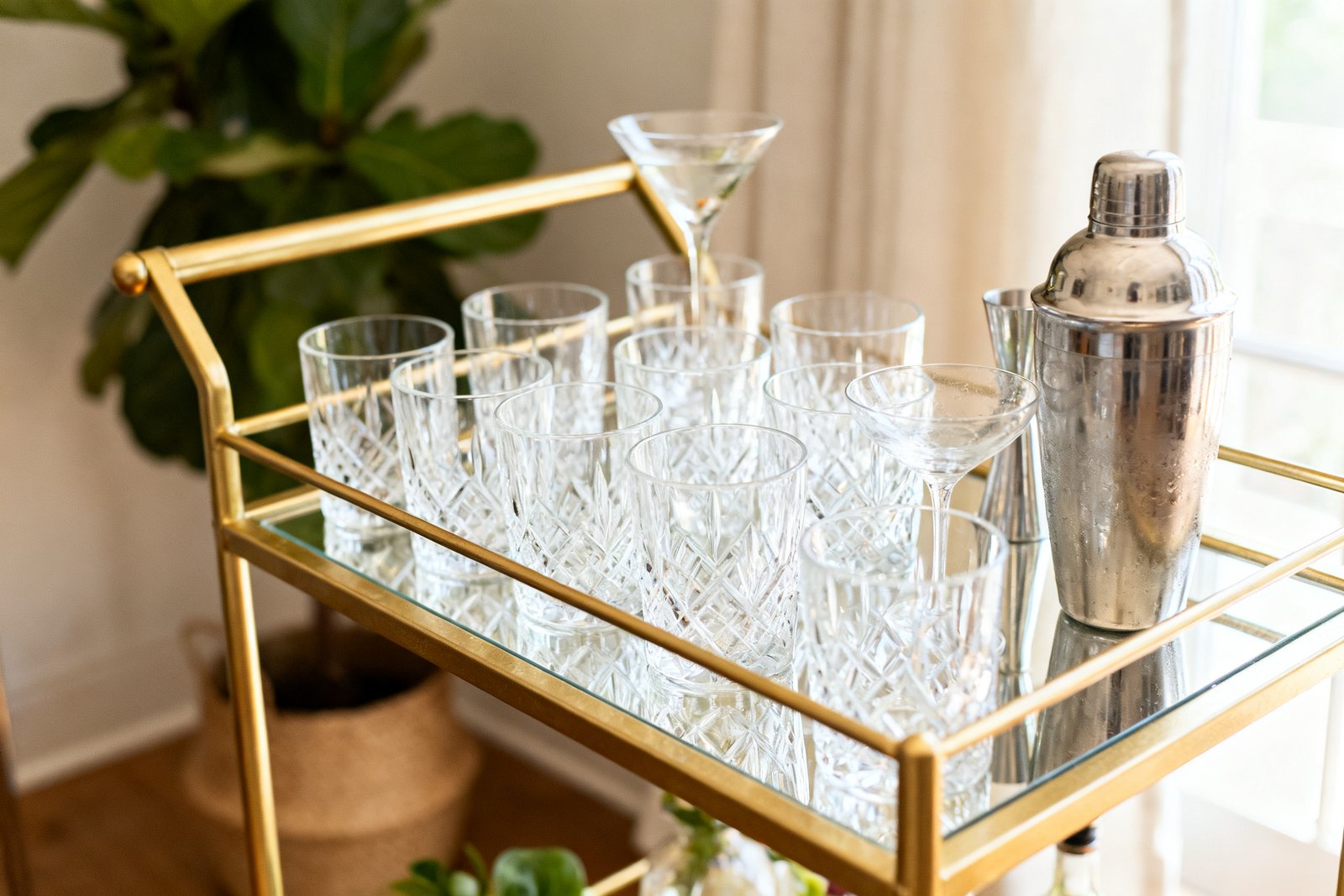 A gold bar cart with neatly arranged glasses and a cocktail shaker