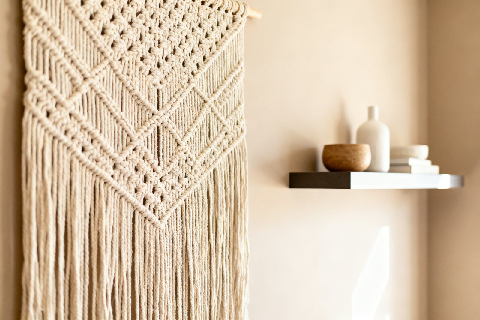 A large woven wall hanging and a floating shelf on a neutral wall